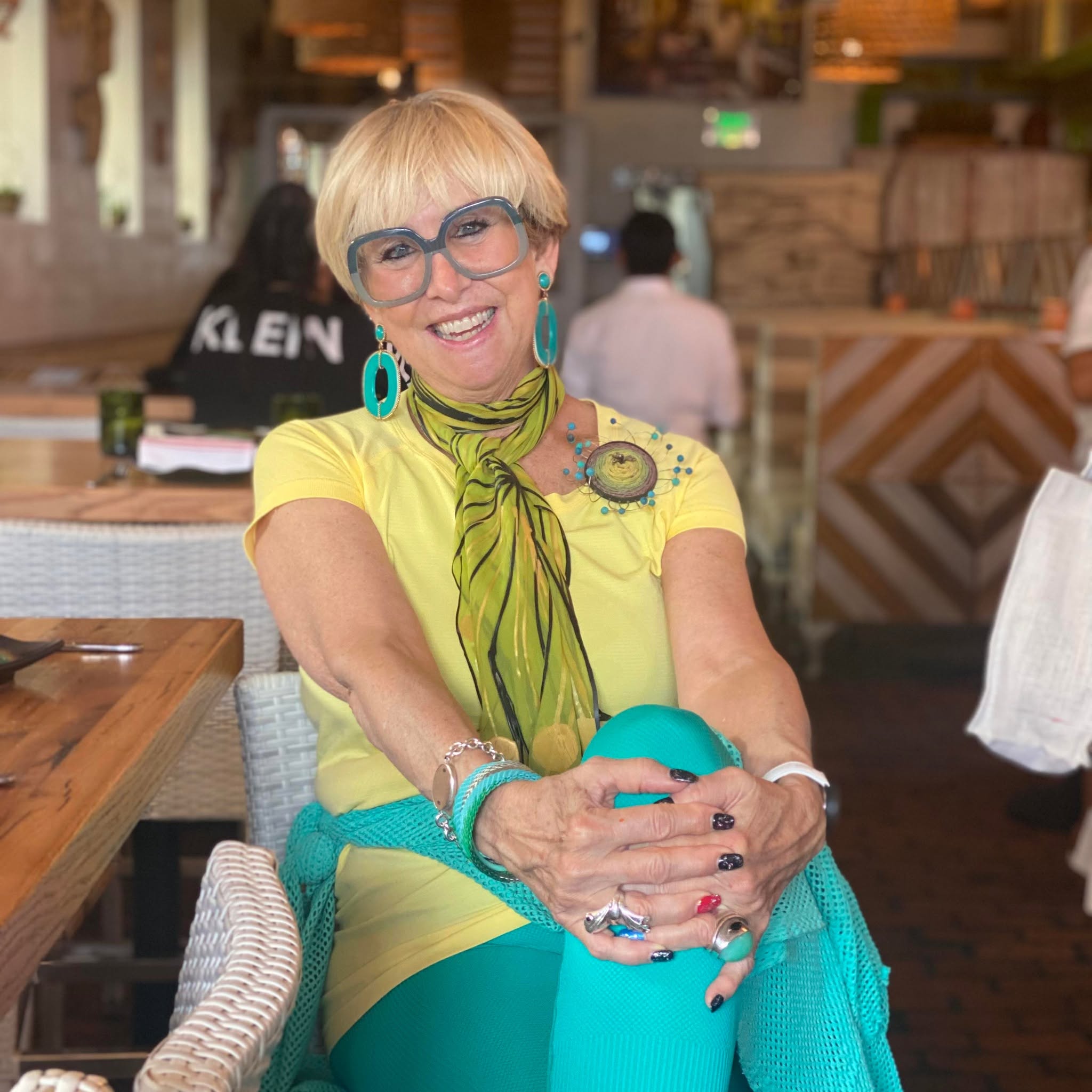 Bonnie Roseman in a yellow top and turquoise accessories, seated