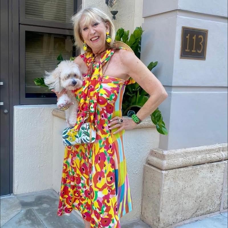 Bonnie Roseman in a floral dress, holding her dog, outside her Palm Beach home